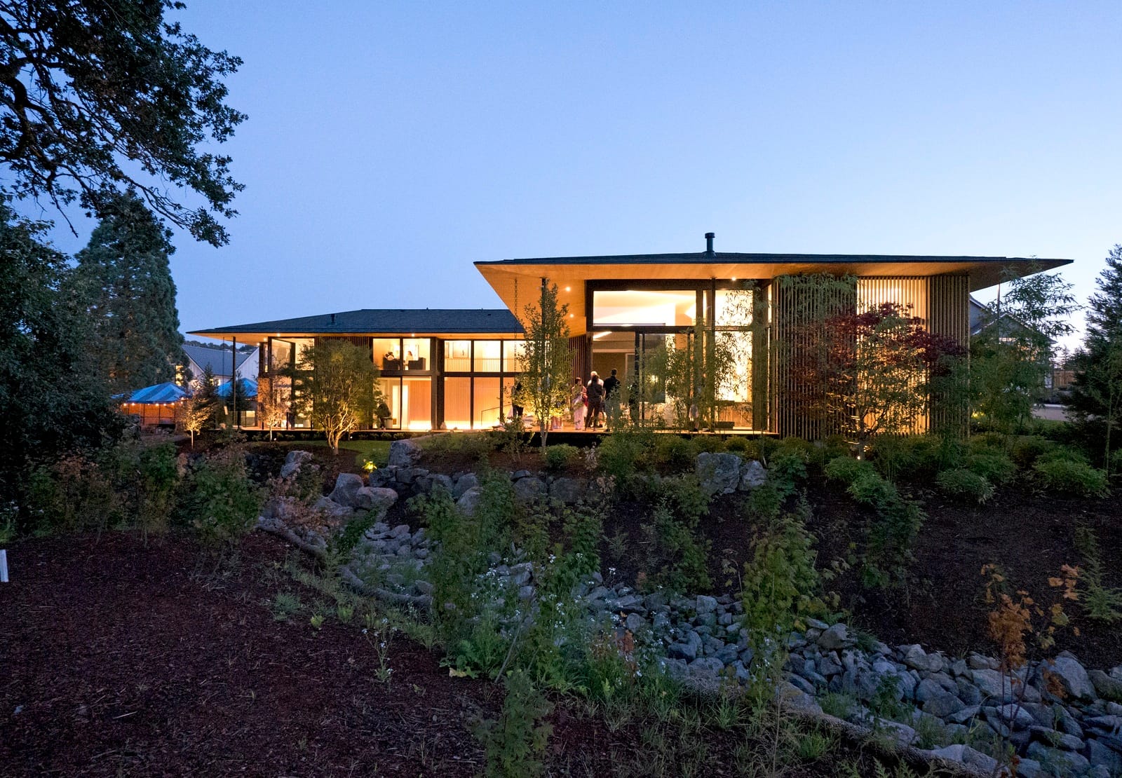 Striking modern Portland, OR home at twilight with timber screens, deep eaves, and a glowing glass-walled interior
